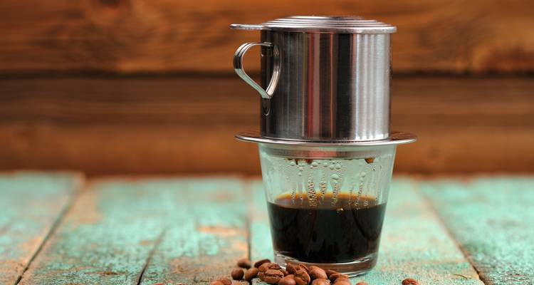 Ein traditioneller vietnamesischer Kaffeefilter auf einem Glas mit Kaffee, auf einem rustikalen Holztisch.
