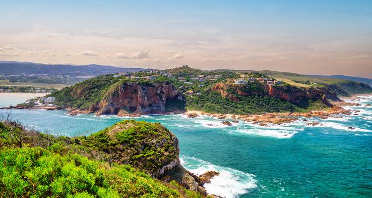 Weelderige groene kaap met rotsachtige kliffen en gebouwen die uitkijken over een uitgestrekte oceaan.