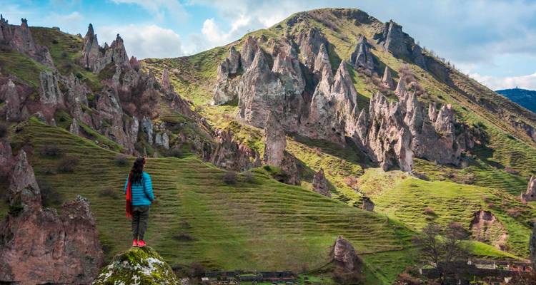 Person, die auf einem grasbewachsenen Hügel steht und auf einzigartig geformte Felsformationen blickt.