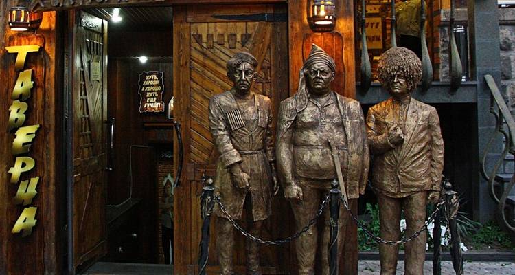 Drei Bronzestatuen vor einem hölzernen Taverneneingang.