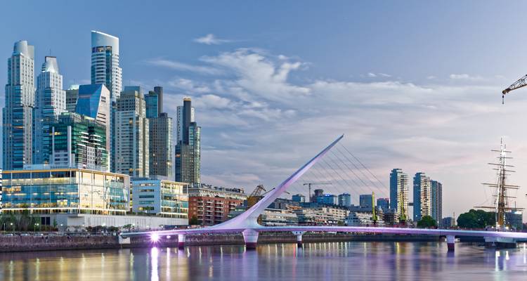 Modern glass skyscrapers and the sleek white Puente de la Mujer bridge reflecting in the calm evening waters of Puerto Madero.