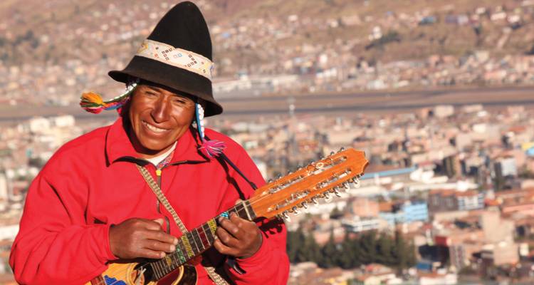 A musician wearing traditional attire playing a guitar with a city in the background.