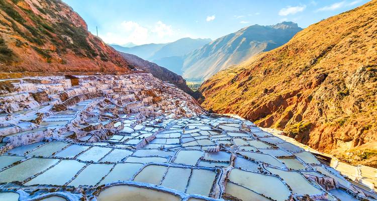 Terrasses vibrantes des salines de Maras scintillant sous un soleil éclatant avec les montagnes des Andes en arrière-plan.
