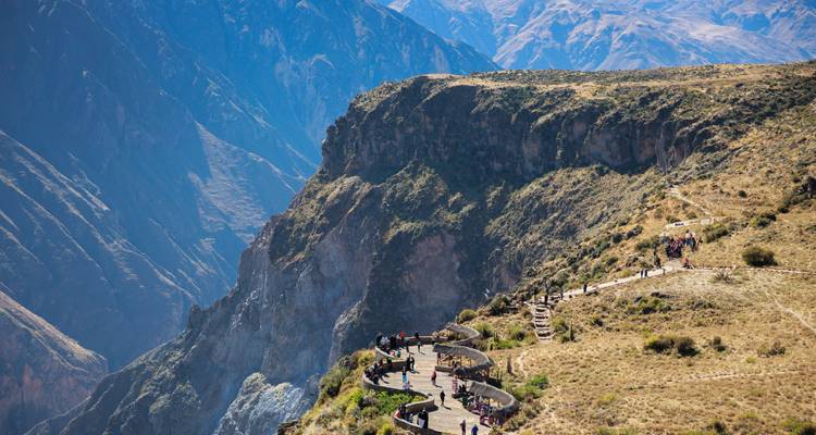 Vue panoramique du canyon de Colca avec des touristes debout sur des plateformes d'observation courbes perchées au-dessus de falaises escarpées.