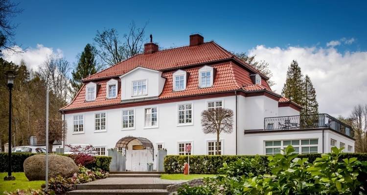 Ein großes weißes Haus mit einem roten Dach in einem gepflegten Garten.
