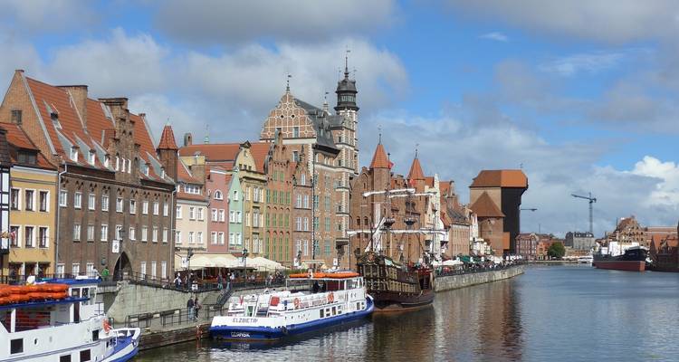 Stadtuferpromenade mit historischen Gebäuden und Booten unter bewölktem Himmel.