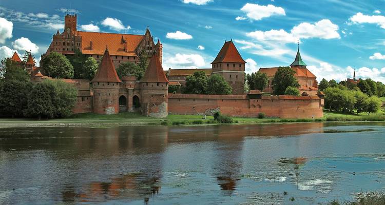Das beeindruckende Schloss Marienburg aus rotem Backstein spiegelt sich in einem ruhigen Fluss wider.