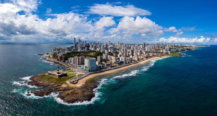 Weitläufiges Luftpanorama von Salvadors Hochhaus-Halbinsel, flankiert von türkisfarbenen Atlantikgewässern und einem historischen Festungsleuchtturm.