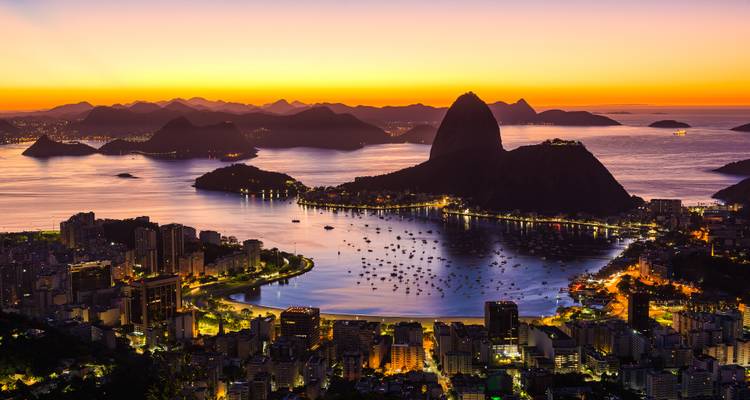 Ikonischer Sonnenuntergang über der Guanabara-Bucht in Rio de Janeiro mit dem Zuckerhut als Silhouette vor goldenem Himmel.