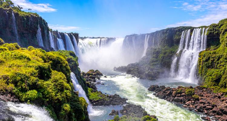 Donnernde Vorhänge der Iguazu-Fälle stürzen durch üppigen Regenwald unter einem strahlend blauen Himmel.
