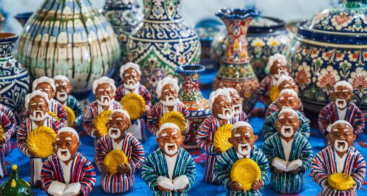 Bunte Keramikfiguren usbekischer Ältester, die an einem Marktstand inmitten von Töpferwaren ausgestellt sind.