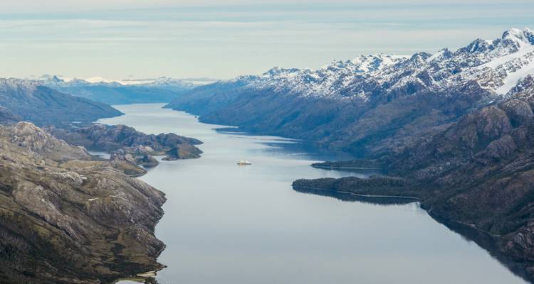 Hoog luchtfoto van een lange slingerende fjord omgeven door ruige, sneeuwbedekte bergketens
