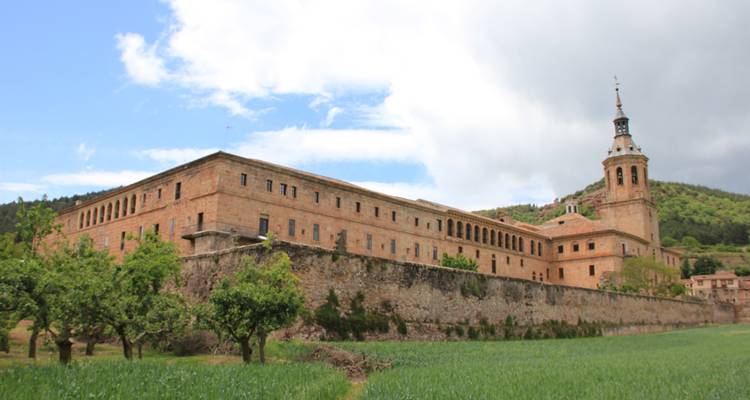 An old monastery building amidst fields and hills in the background.