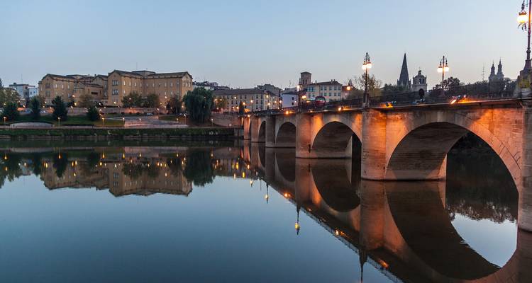 Panoramic view of a bridge over a calm river with reflections at dusk.