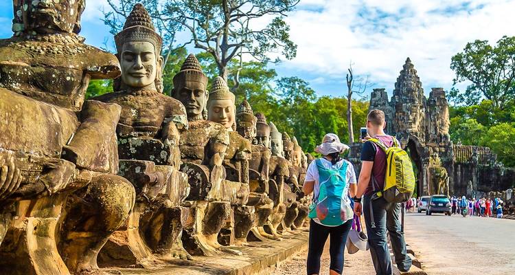 Des touristes marchant le long d'un sentier bordé de statues de pierre, se dirigeant vers une porte de temple.
