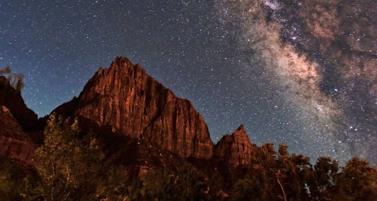 Cielo nocturno con estrellas sobre un paisaje montañoso.