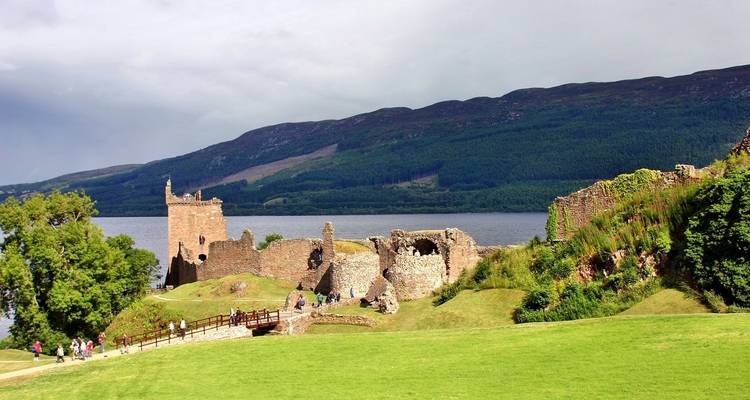 Ruinas de un castillo histórico junto a un lago con gente explorando.