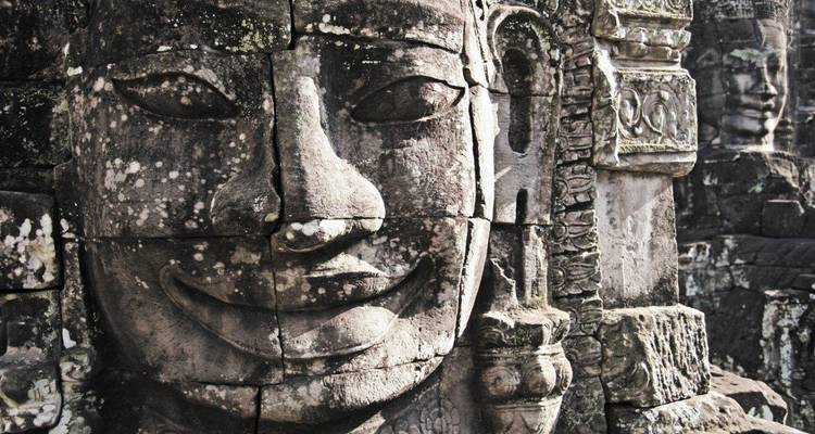 Alte Steinschnitzereien von lächelnden Gesichtern an einer Tempelstruktur.