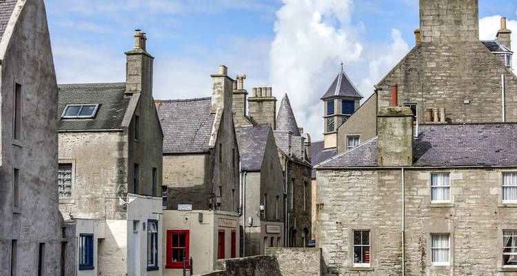 Des maisons de ville en pierre grise aux toits d'ardoise bordent une rue étroite et calme sous un ciel bleu