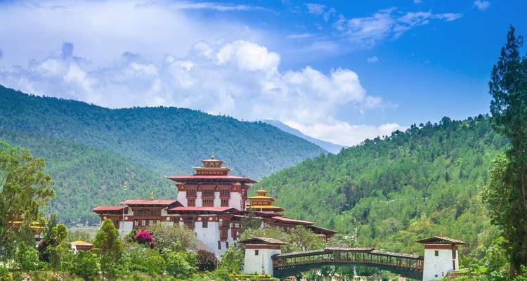 View of Punakha Dzong, a large Bhutanese fortress-architecture building surrounded by lush greenery and mountains.