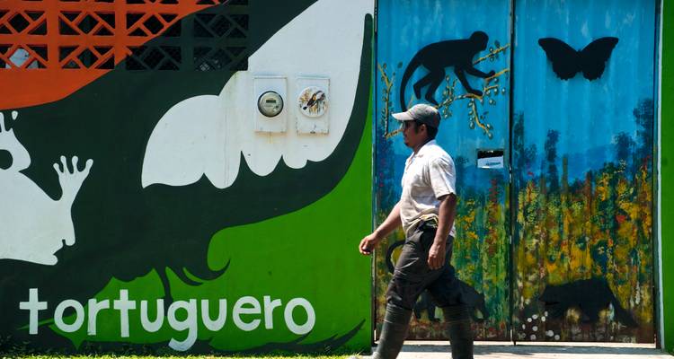 Fresque murale colorée portant l'inscription « tortuguero » avec des silhouettes de faune sauvage alors qu'un homme en bottes marche devant.