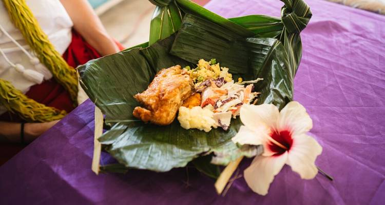 Traditional Samoan meal of chicken, salads and root vegetables wrapped in a banana leaf on a purple cloth.