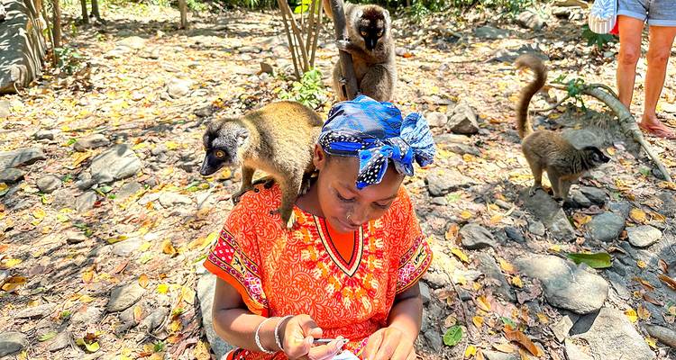 Una mujer sentada con lémures en sus hombros en un entorno natural.