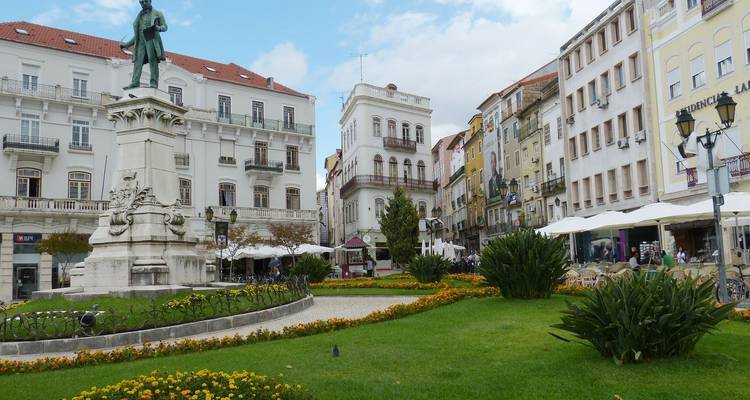 Una plaza de la ciudad con una estatua en el centro, rodeada de edificios históricos y cafés al aire libre.