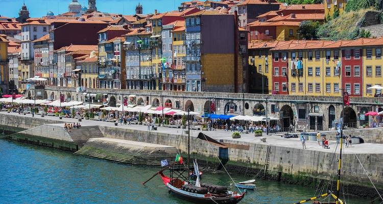 Un pintoresco paseo ribereño con edificios coloridos y una embarcación tradicional en el agua.