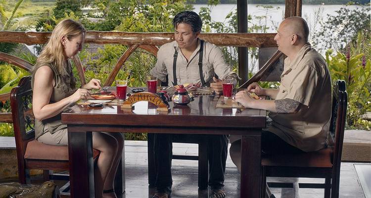Tres personas cenando en una mesa de madera con una vista panorámica de fondo.