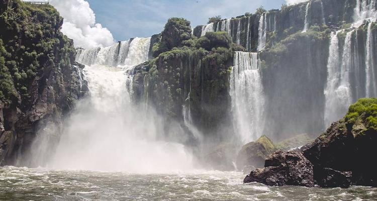 Aufwärtsblick auf einen breiten Iguazu-Wasserfall, der in einen brodelnden Fluss inmitten einer felsigen Schlucht stürzt.