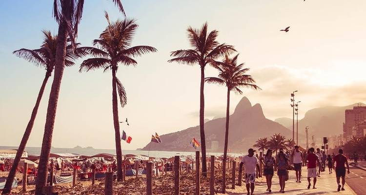 Ikonischer Ipanema-Strand mit Palmenreihe und Badegästen vor Rios Bergen in der Abenddämmerung