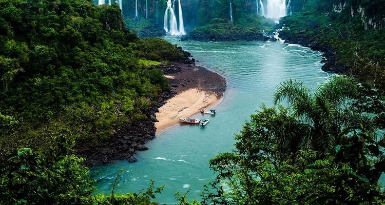 El río color turquesa se encuentra con una cala arenosa y la selva densa debajo de las imponentes Cataratas del Iguazú.