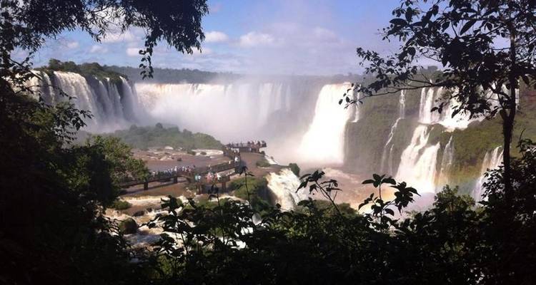 Un marco natural de follaje revela la inmensa cortina de las Cataratas del Iguazú bajo cielos azules.