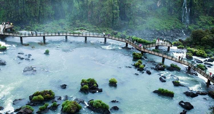 Los turistas se alinean en un puente peatonal curvo sobre las aguas azules y remolineantes cerca de las Cataratas del Iguazú.