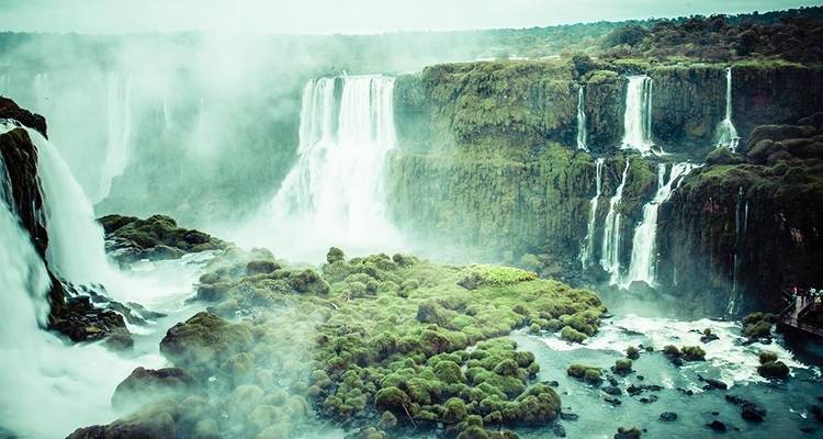 La niebla se eleva desde varios grandes saltos de las Cataratas del Iguazú enmarcados por acantilados de color esmeralda.