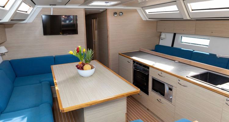 Salon de yacht lumineux avec sièges bleus, table à manger, cuisine complète et baies vitrées.