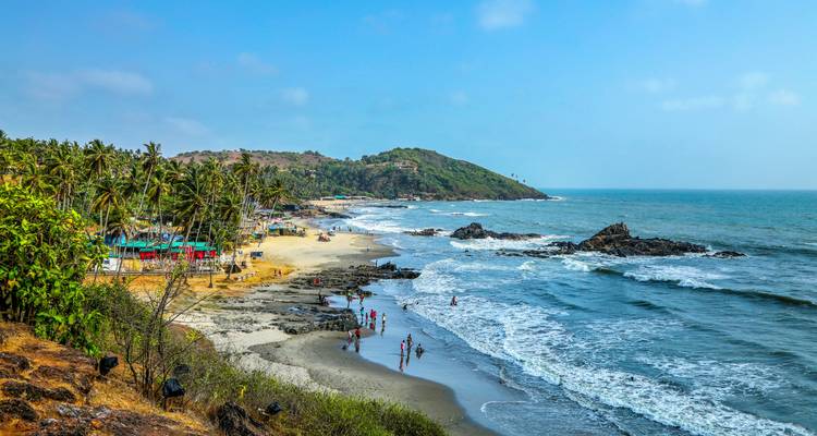 A scenic beach view with people enjoying the shoreline and waves in Goa.