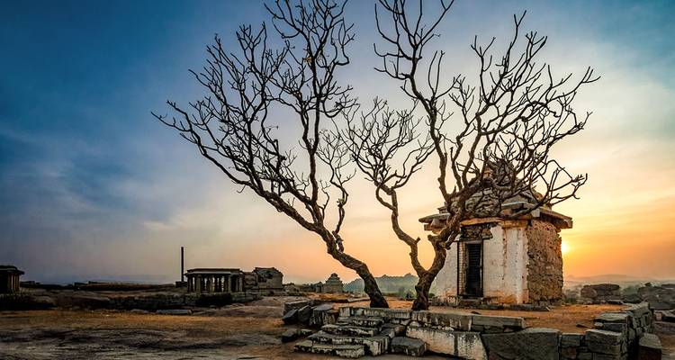 Kleiner Tempel und ein kahler Baum vor einer Sonnenaufgangs-Kulisse.