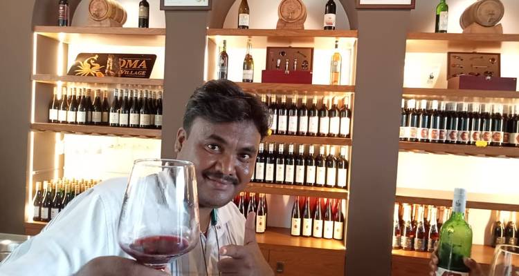 Man holding a wine glass in a winery with bottles lined up behind.
