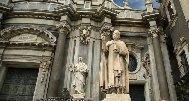 Façade de cathédrale baroque ornée avec de grandes statues et des colonnes en marbre sur un ciel morose.