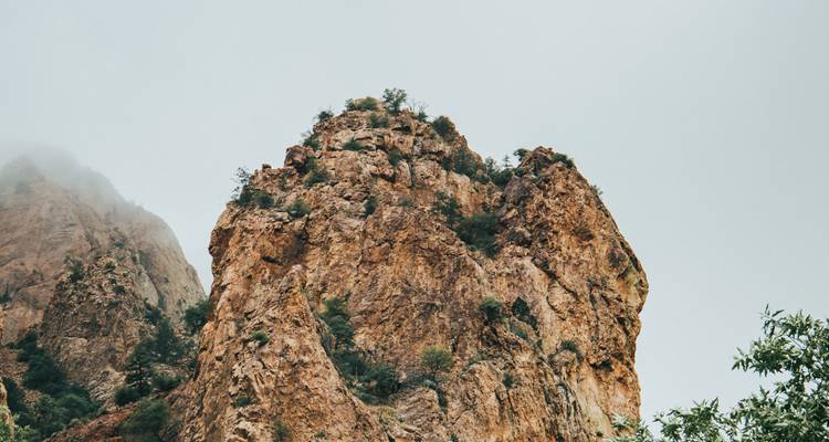 Felsiger Gipfel mit Baumbedeckung unter bewölktem Himmel.