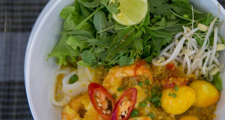 Nahaufnahme einer Schüssel vietnamesischer Nudelsuppe mit Garnelen und Kräutern.