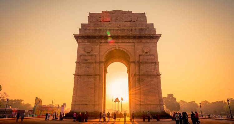 Los visitantes silueteados caminan bajo la India Gate mientras el sol naciente se alinea con el arco.