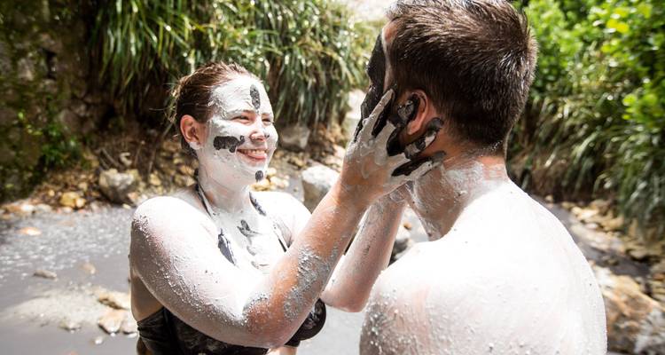 Pareja sonriendo mientras se aplican barro volcánico blanco el uno al otro en un spa natural.