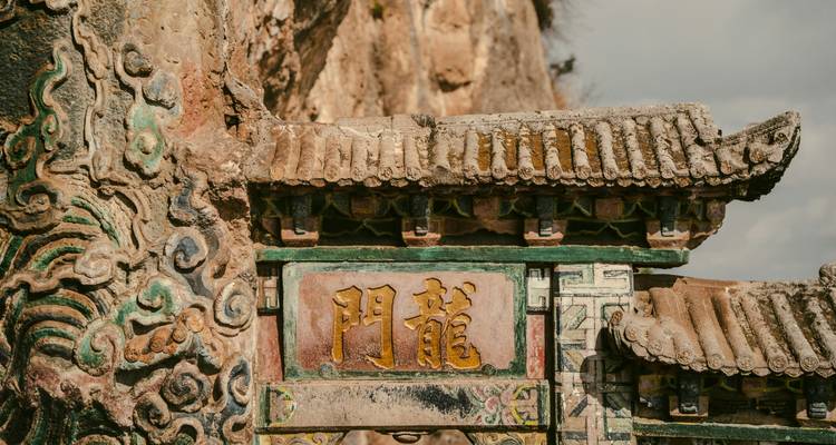 Puerta de piedra desgastada con caracteres chinos y ornadas tallas de dragones en la Puerta del Dragón, Kunming.