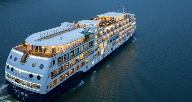 Luxury multi-deck river cruise ship sails along calm blue water at dusk.
