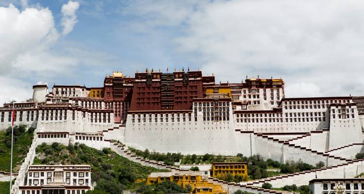 The grand Potala Palace rises atop its hill against a bright blue sky and drifting clouds.
