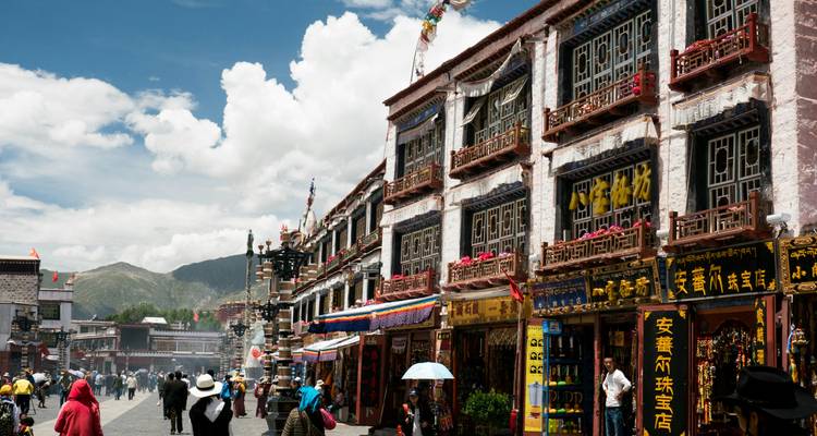 Bustling Tibetan street lined with colorful shopfronts, pilgrims and wafting incense smoke.
