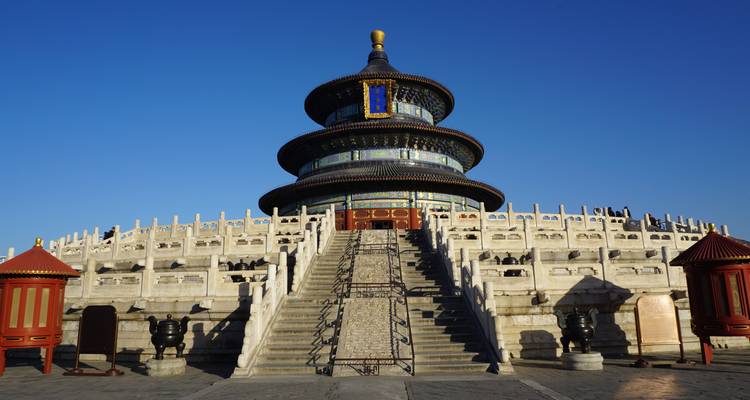 Symmetrical view up the staircase to the circular Temple of Heaven under a deep blue sky.